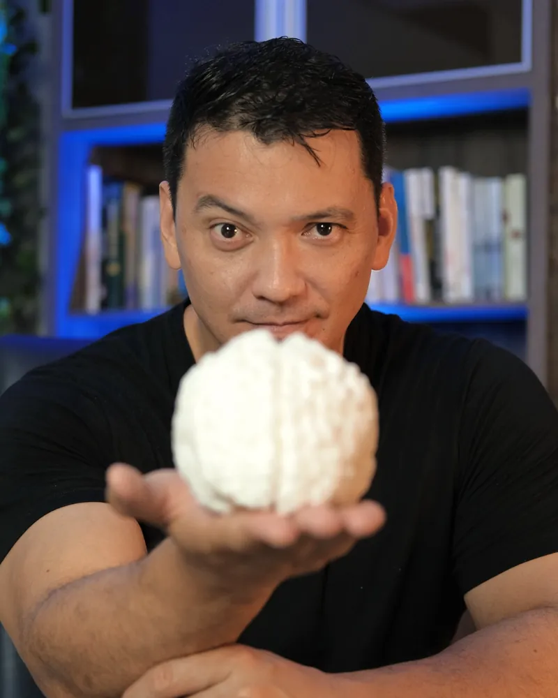 Luciano Tokikawa segurando uma réplica de cérebro, referência à base em neurociência da Perpetuação